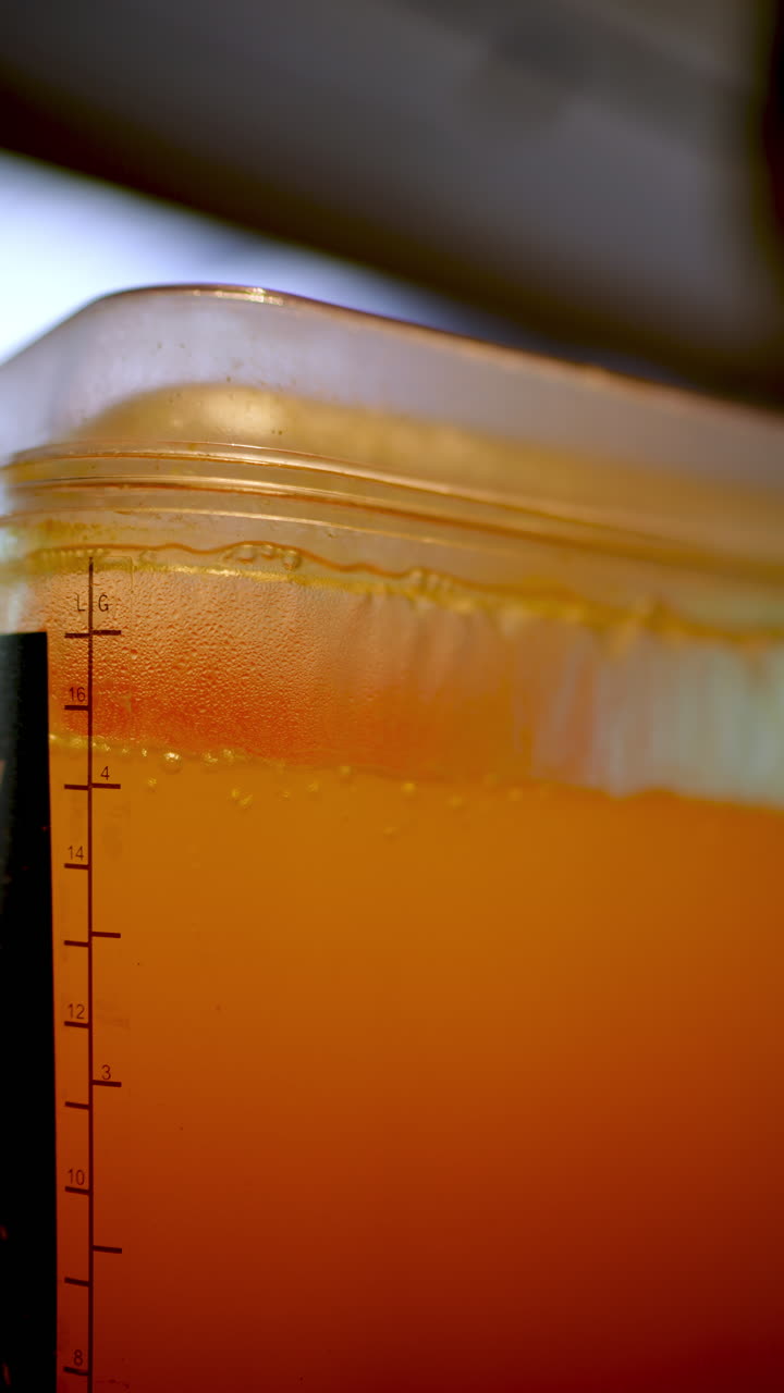 Closeup of orange liquid with bubbles inside a transparent container with measurement scale and plastic lid