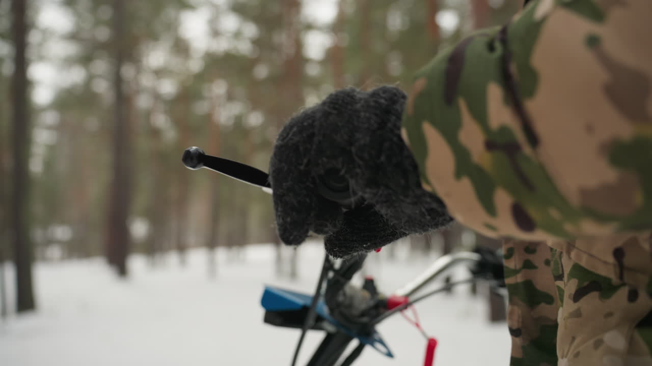 Hanskekledd hånd på ATV-gass i furuskog, nærbilde av grep og tenning, rask akselerasjon og vibrasjon, fører styrer maskinen gjennom en smal trekorridor, snøsprut og flygende pudder, dynamisk