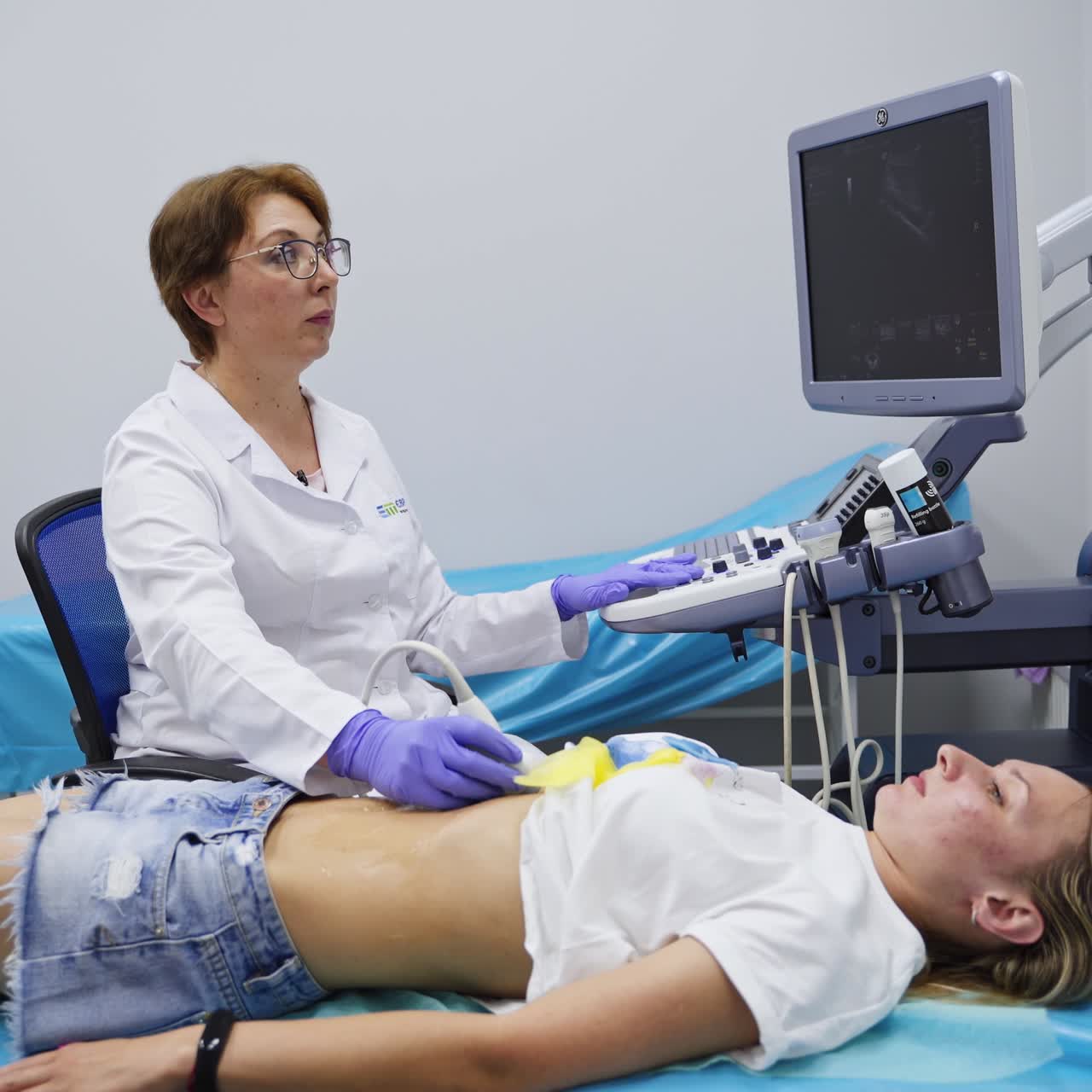 Woman lies on the couch of the physician carrying out the ultrasonic check. Female doctor looks at the screen and moves the transducer