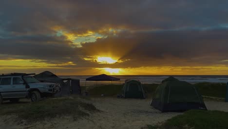 Vista-Del-Amanecer-Sobre-Un-Camping-Tranquilo-Junto-A-La-Playa-En-Las-Dunas-De-La-Isla-Fraser-De-Queensland,-Con-Camiones-4x4-Y-Tiendas-De-Campaña-Ondeando-Suavemente-En-La-Brisa-De-La-Mañana