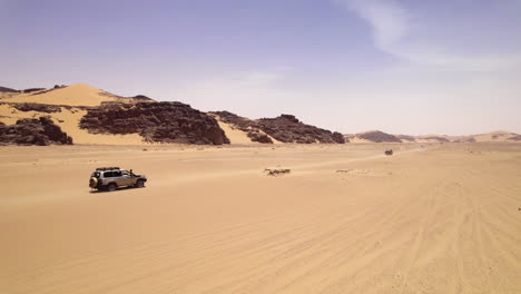 vehicles driving along the sand dunes of djanet desert in algeria - drone shot