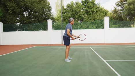 Video-of-biracial-senior-man-holding-racket-and-starting-match-on-tennis-court