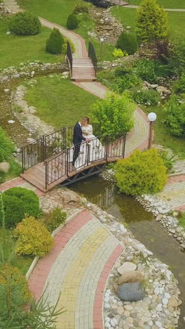 happy just married couple on little bridge over stream in green park on warm sunny day aerial view