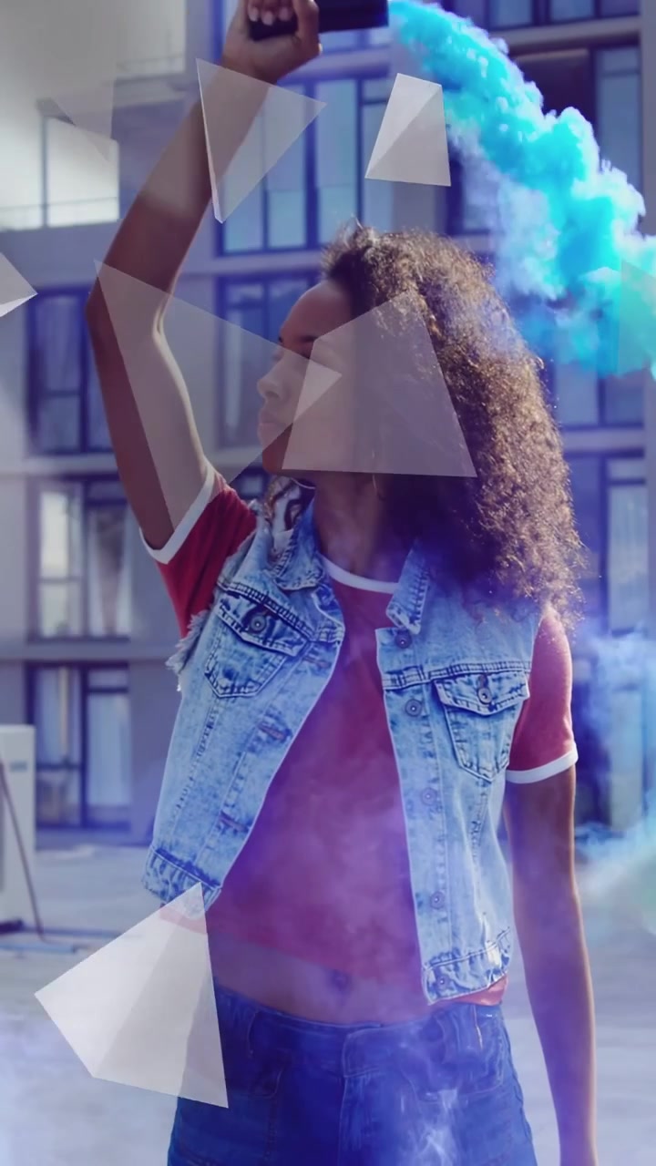 Video verticale: Donna che alza un fumogeno, emettendo fumo blu, triangoli che fluttuano sopra di lei per un servizio fotografico artistico.