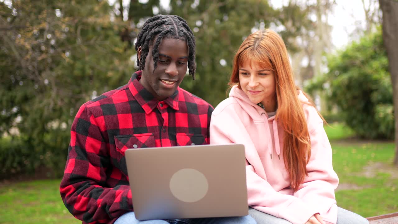 Two students working on a laptop in the park