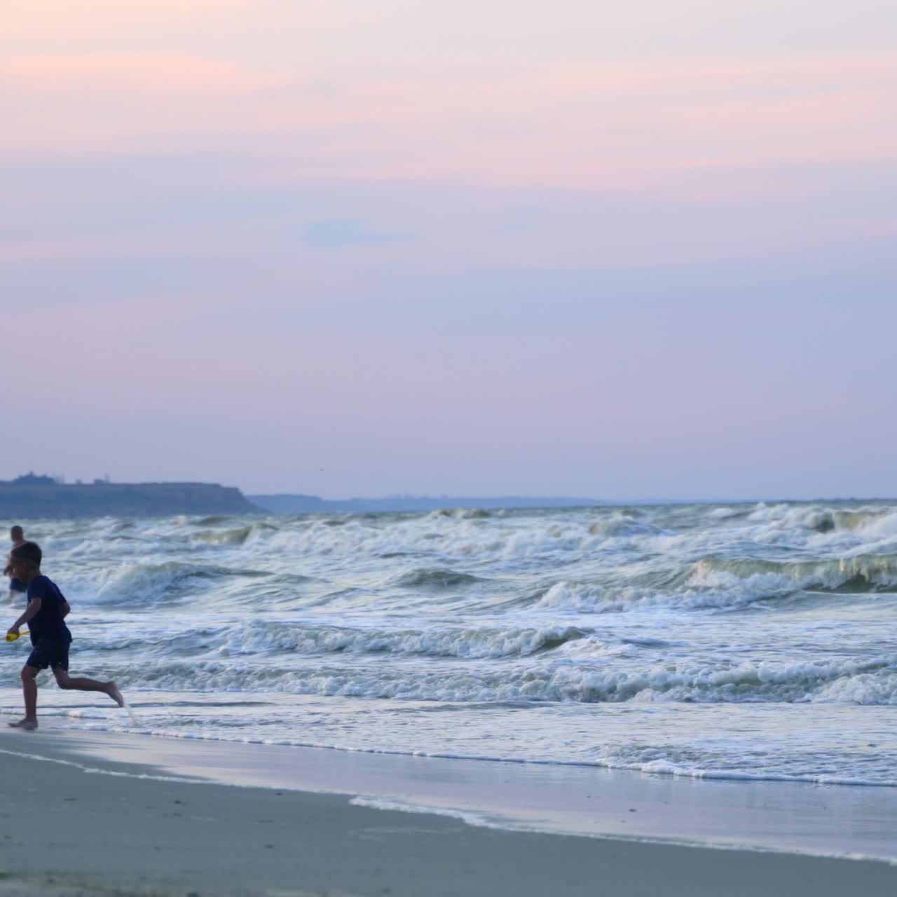 Little boy playing with water in the seashore. Cute child enjoys with his toy near the water in the evening. Happy childhood.