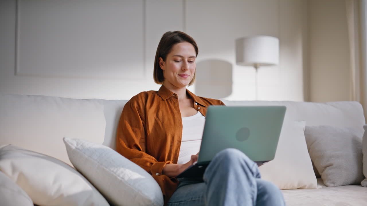 Serene freelancer reading email at laptop sitting comfortable apartment sofa