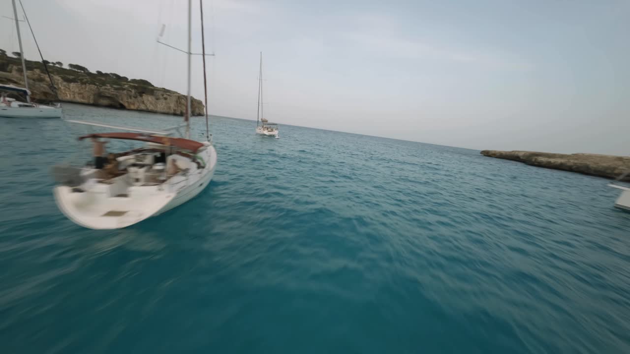 vuelo con drones fpv sobre los veleros atracados a lo largo de la costa con espectaculares acantilados en cala varques, mallorca, españa durante la noche