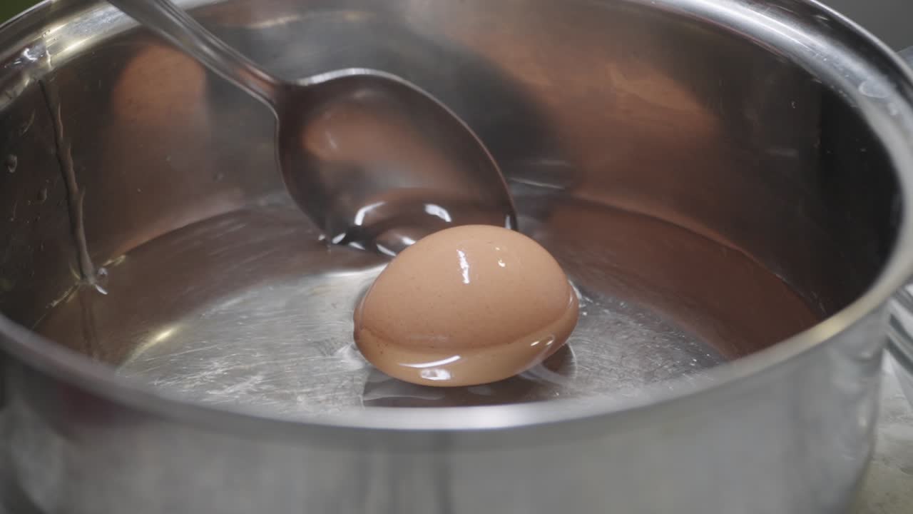 Ei voorzichtig met een lepel in water in een steelpan geplaatst, close-up van het kookproces.