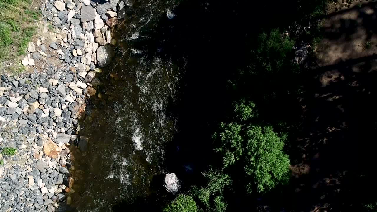 un pescador con mosca se revela mientras el río fluye pesadamente junto a una carretera mientras el dron desciende y los autos pasan