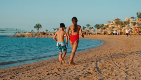 Barfüßige-Kinder-Vergnügen-Sich-Bei-Sonnenuntergang-Am-Meeresufer.-Geschwister-Laufen-Am-Meeresstrand