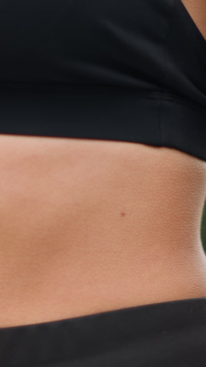 Close-up view of a woman's stomach with goosebumps as she breathes in deeply, showing her physical response to a deep breath while wearing black workout gear, focusing on her midsection