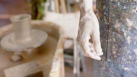 dirty hand of biracial male potter, standing in pottery studio, slow motion