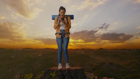 full body of asian female hiker with mountaineering backpack looking at the smartphone and saying wow while standing on the top of mountain during sunset time