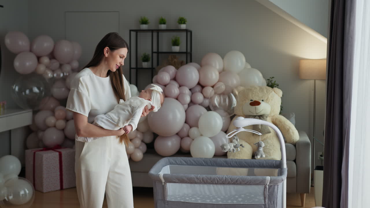 Madre culla teneramente il neonato tra palloncini festivi e un orsetto di peluche, in una cameretta accogliente