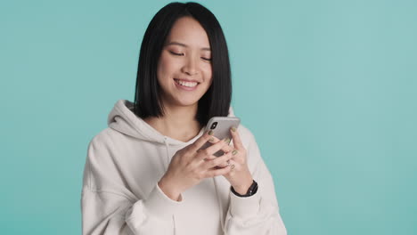 asian woman texting on smartphone and laughing on camera.