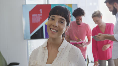 Portrait-of-happy-biracial-businesswoman-over-diverse-colleagues-in-office