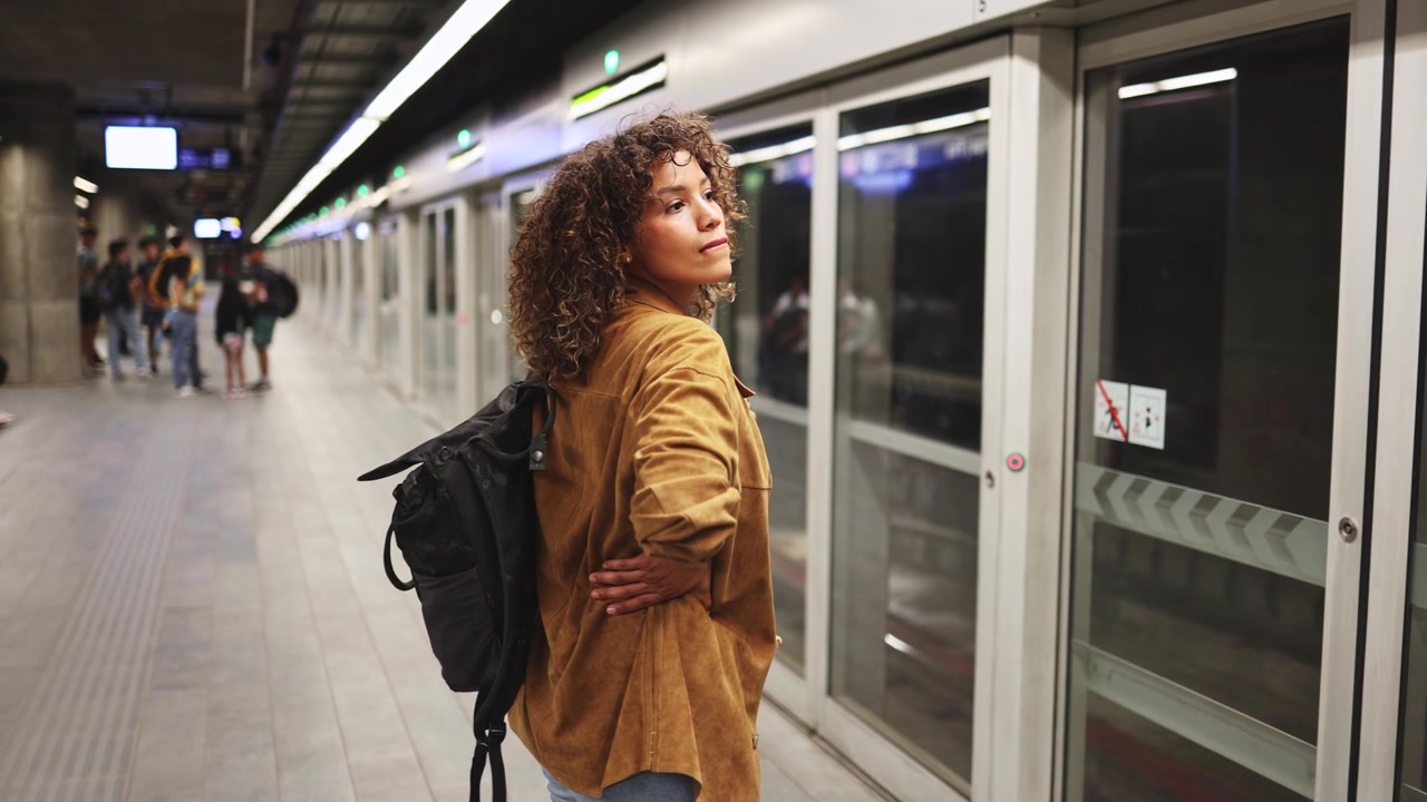 Giovane donna con zaino che aspetta sulla banchina della metropolitana.