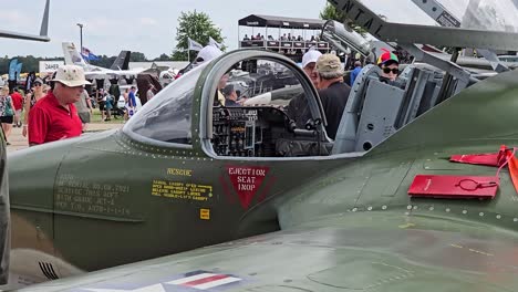 close-up of a vintage military aircraft cockpit with ejection seat warning labels, displayed at eaa airventure in oshkosh, wi. attendees observe in the background.