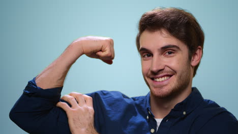 young man showing biceps on blue background. strong man posing at camera