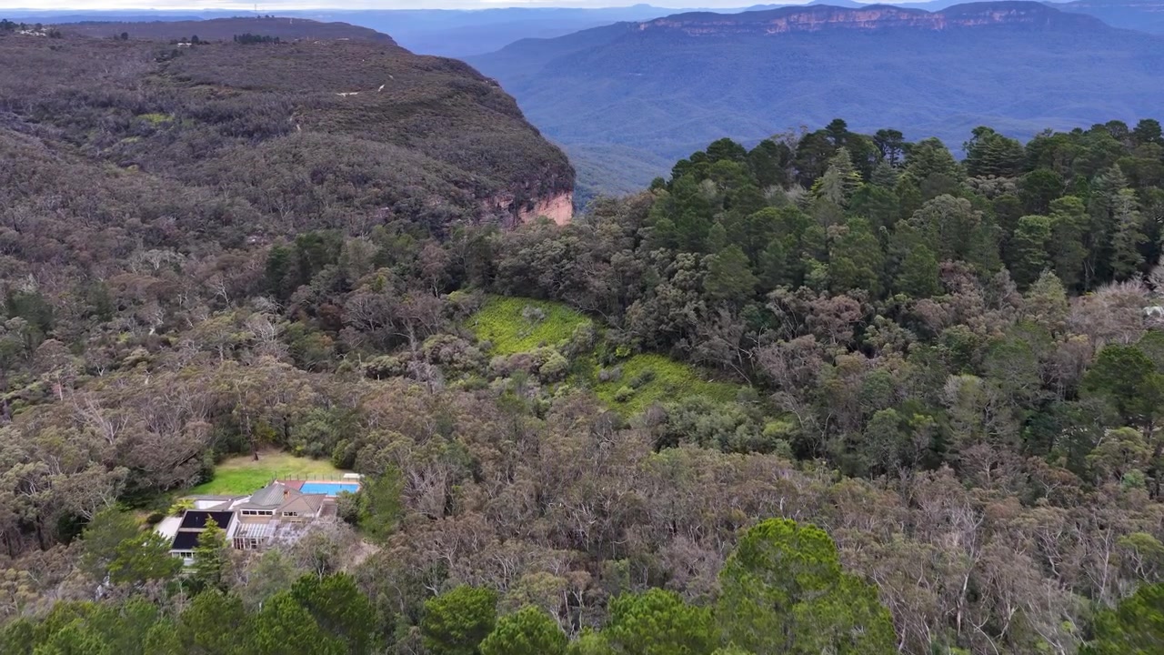 Imagem de drone sobrevoando exuberante floresta de eucaliptos em direção a falésias de arenito em Wentworth Falls, Austrália.