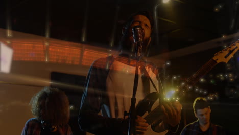 bandmates performing music under warm lights, singing into mic and strumming guitars with city glow
