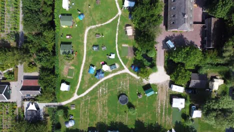 grass field camping site with vehicles, caravans and tents, aerial