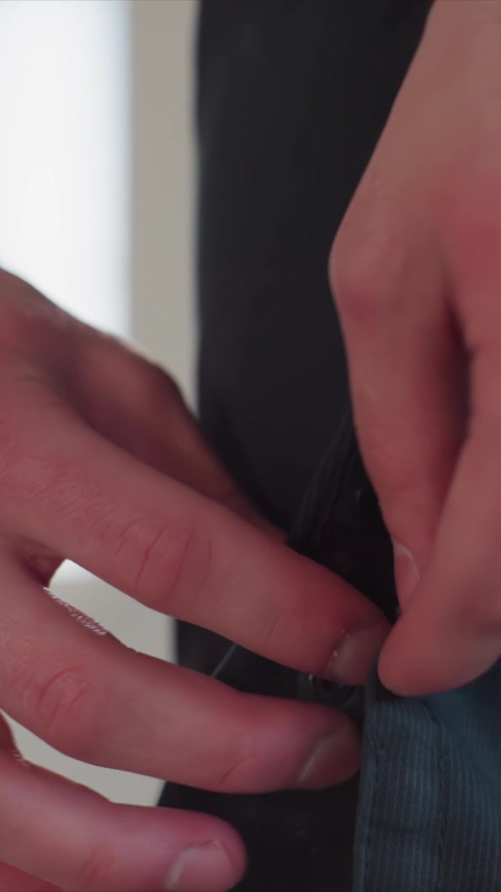 Close up of man hands adjusting dark clothing manipulating. Hands interact with buttons snap closures blue denim material. Hands carefully align seams smooth out garment ensuring