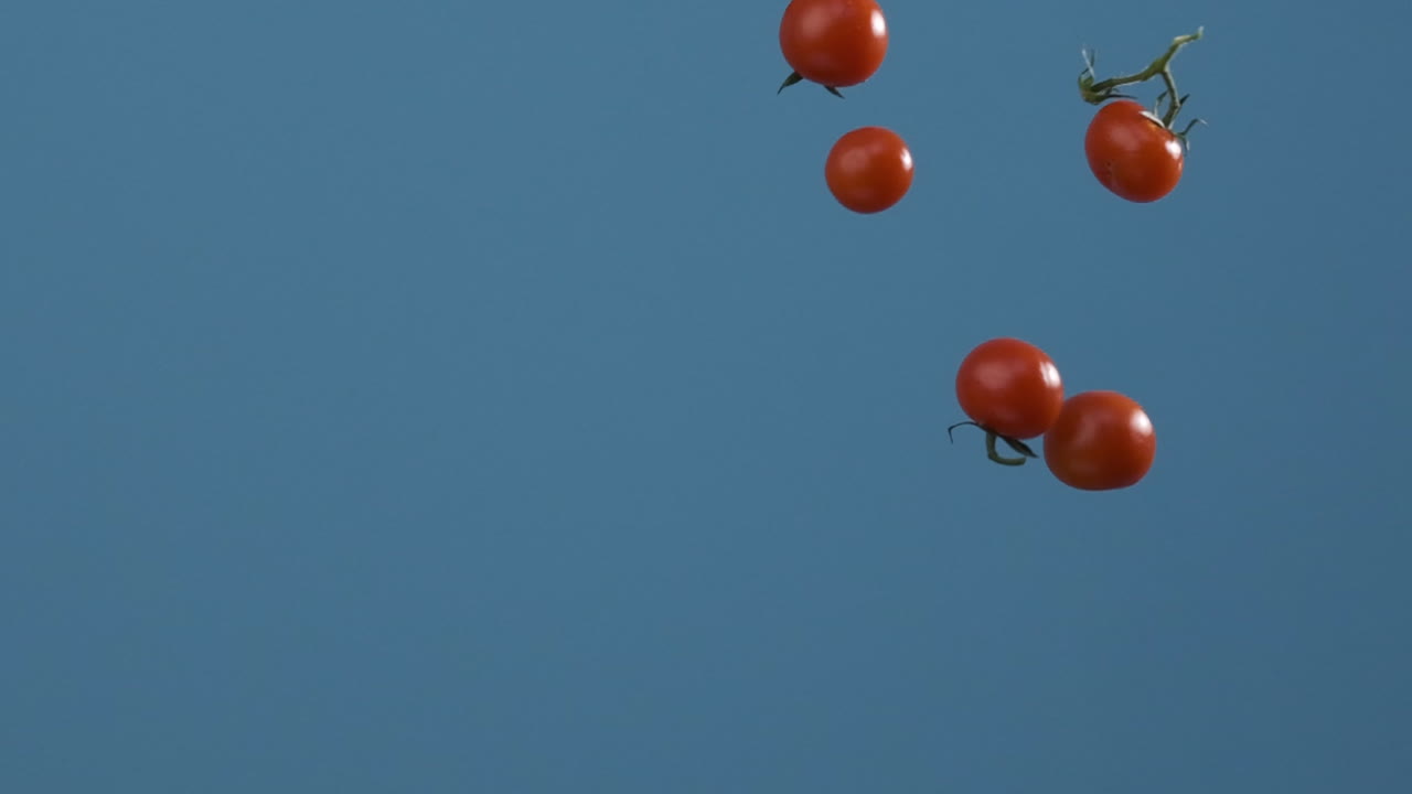Falling Cherry Tomatoes with Water Droplets on Blue Background