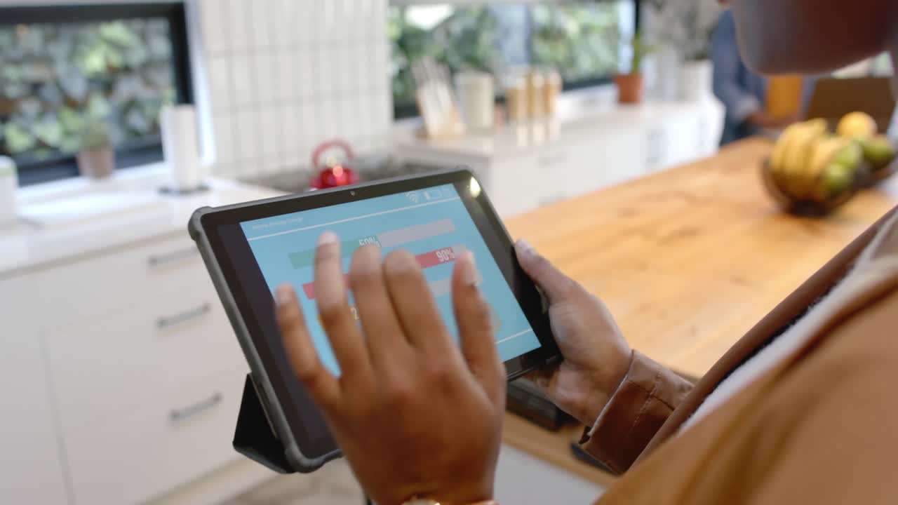 Mid section of african american woman using tablet with smart home interface in kitchen, slow motion
