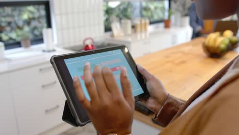 Mid-section-of-african-american-woman-using-tablet-with-smart-home-interface-in-kitchen,-slow-motion