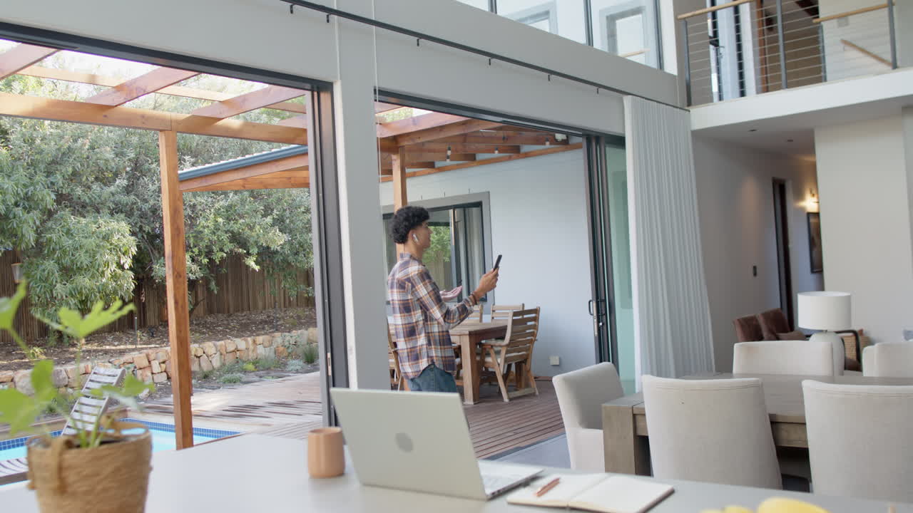 Using smartphone, teenage boy walking in modern home with open sliding doors