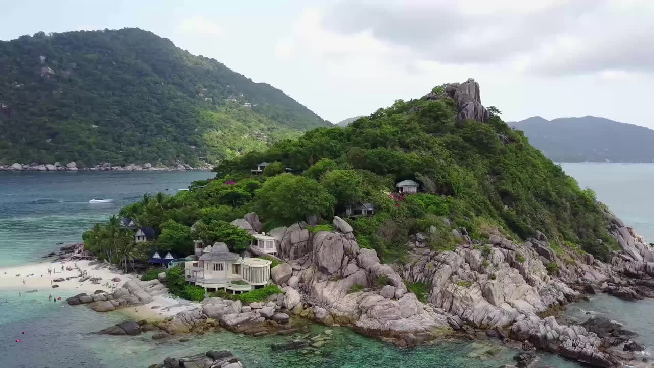 A small tropical island overgrown with rainforest with small houses on it. Upwards panning. Koh Tao. Thailand