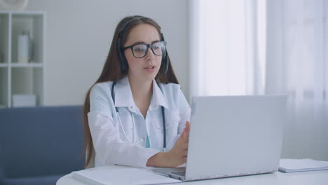 Doctora-India-Trabajadora-Haciendo-Videollamadas-En-Una-Computadora-Portátil-En-El-Hospital.-Una-Joven-Doctora-Sonriente-Usa-Un-Estetoscopio-Uniforme-Blanco-Consultando-A-Un-Paciente-En-Línea-A-Través-De-Una-Videollamada