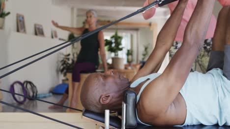 focused diverse seniors stretching in pilates class with female coach, unaltered, in slow motion