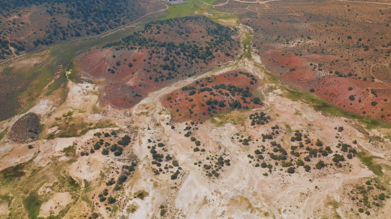 Diverse colors of dry landscape with scarce greenery. Some cabins and roads at backdrop. Aerial perspective.