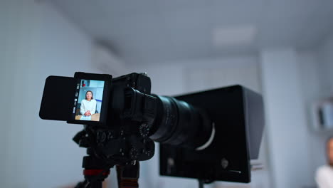 beautiful woman on the display of professional camera. distancing from equipment recording blog content. blurred backdrop.