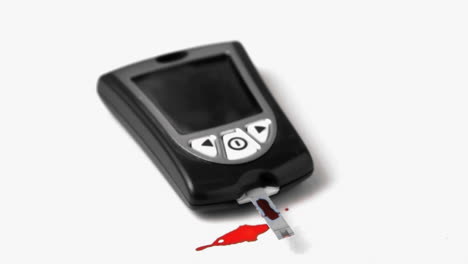 drop of blood falling onto test strip of blood glucose monitor on white background