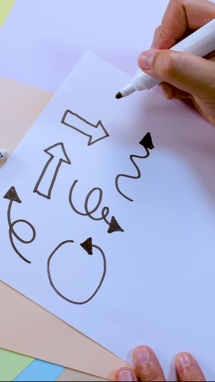 Person draws various arrows and shapes on white paper using black marker, overhead view