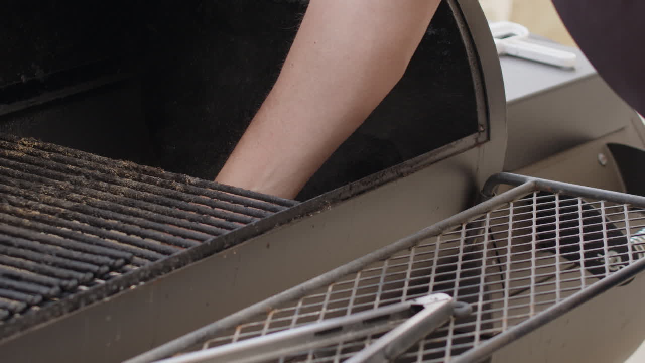 Man cleaning ash from BBQ grill with shovel before cooking