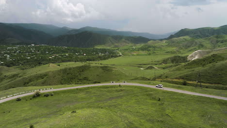 Coche-Todoterreno-Blanco-Conduciendo-Por-La-Carretera-Con-Vistas-Panorámicas-De-Verdes-Praderas-Y-Montañas-En-Verano-En-Georgia