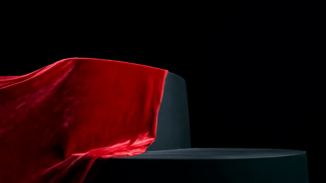 Una mano nascosta che tira un telo di velluto rosso fuori dallo schermo, rivelando un piedistallo a due livelli in studio