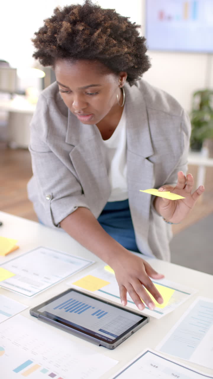 Vertical video of african american casual businesswoman making notes in office, slow motion
