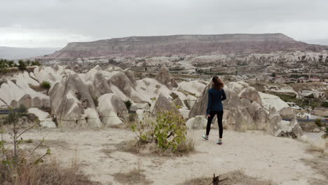 Drone-following-a-woman-to-the-cliffs-edge-to-reveal-the-fairy-chimneys-and-fast-landscape-of-Goreme-Turkey