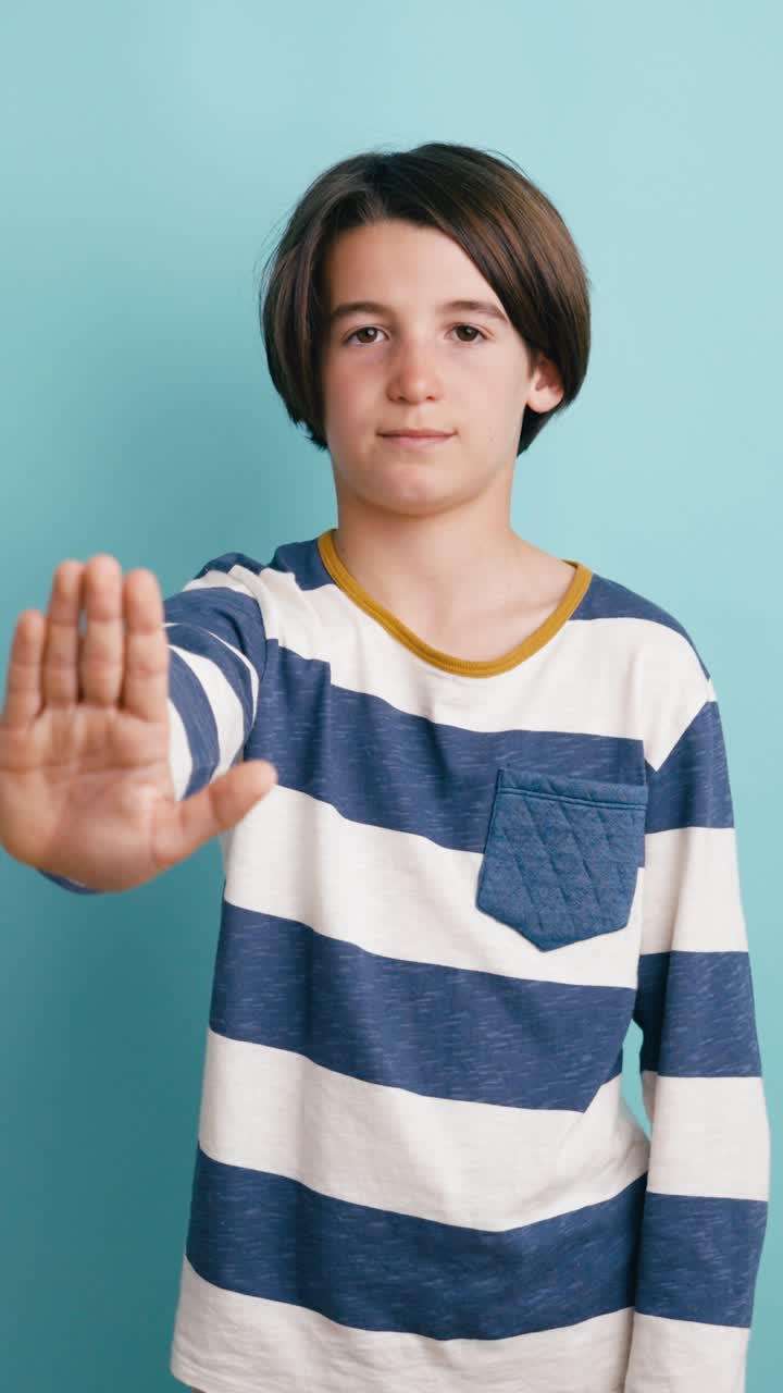 Giovane ragazzo che fa un gesto di stop con la mano su sfondo blu.