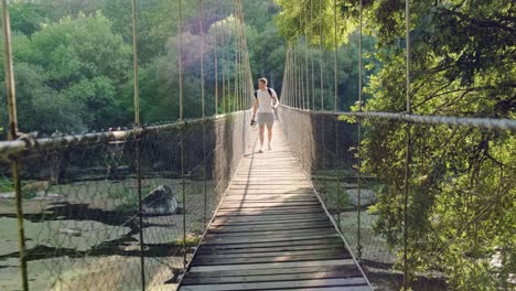 caucasian male crossing suspension bridge over river calm water in national park, slow motion