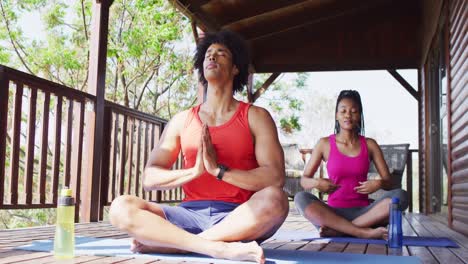 feliz pareja afroamericana haciendo yoga y meditando en una cabaña de madera, cámara lenta