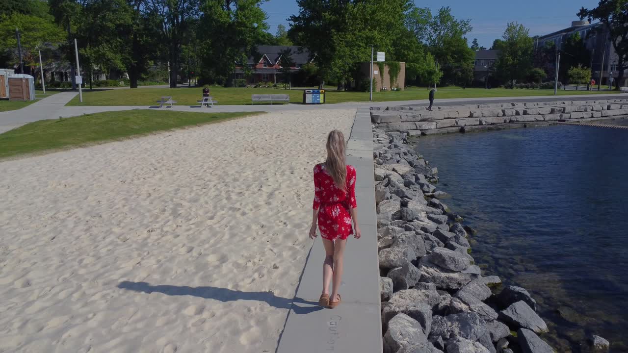 귀여운 빨간 드레스를 입고 해안가를 따라 걷는 젊은 여성의 추적 샷