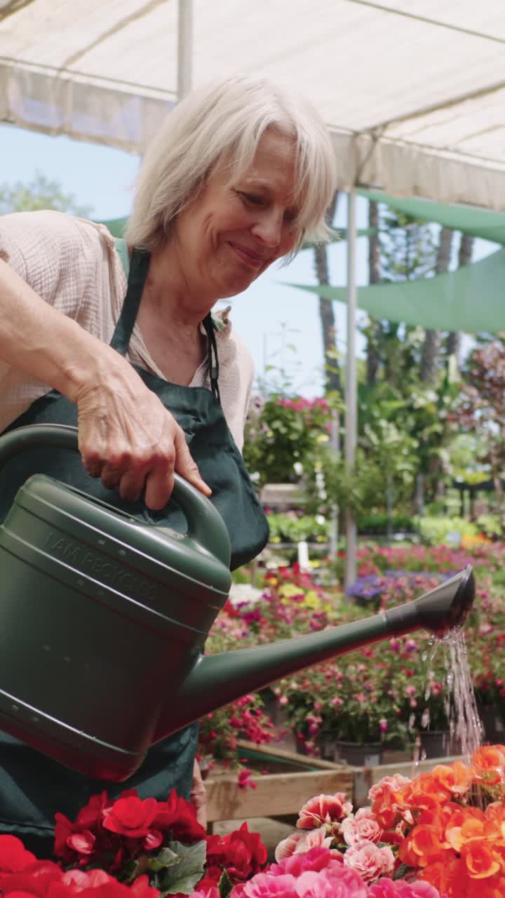 Senior woman watering flowers in a greenhouse