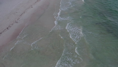 aerial top down shot of rolling waves in a crystal clear white sand beach in cancun, mexico